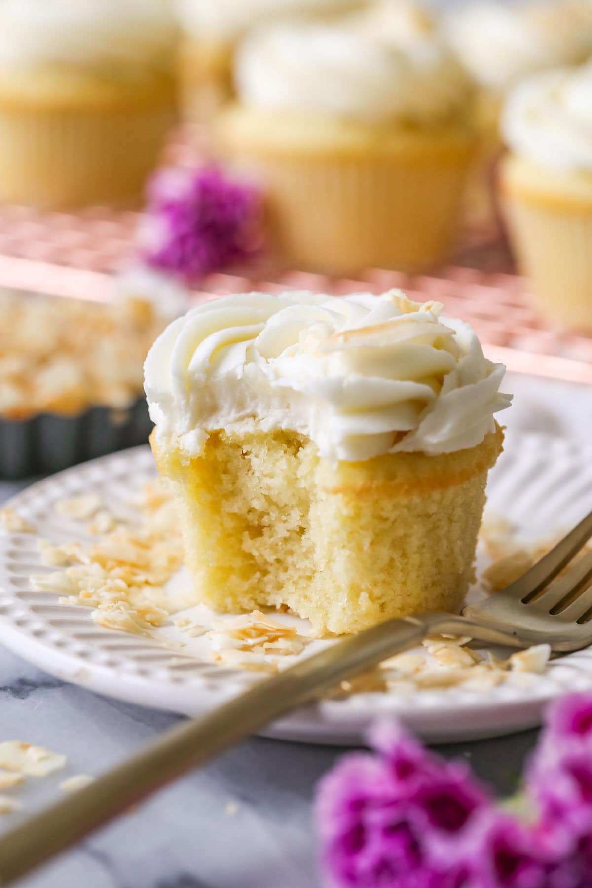 Bite missing from a cupcake topped with a swirl of coconut cream cheese frosting and toasted coconut.