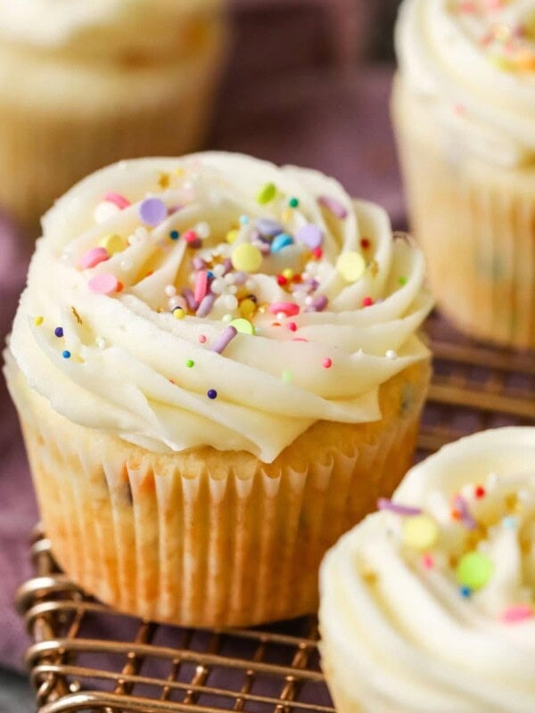 Confetti cupcakes topped with buttercream swirls and sprinkles on a cooling rack.