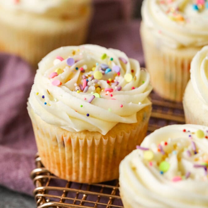 Confetti cupcakes topped with buttercream swirls and sprinkles on a cooling rack.