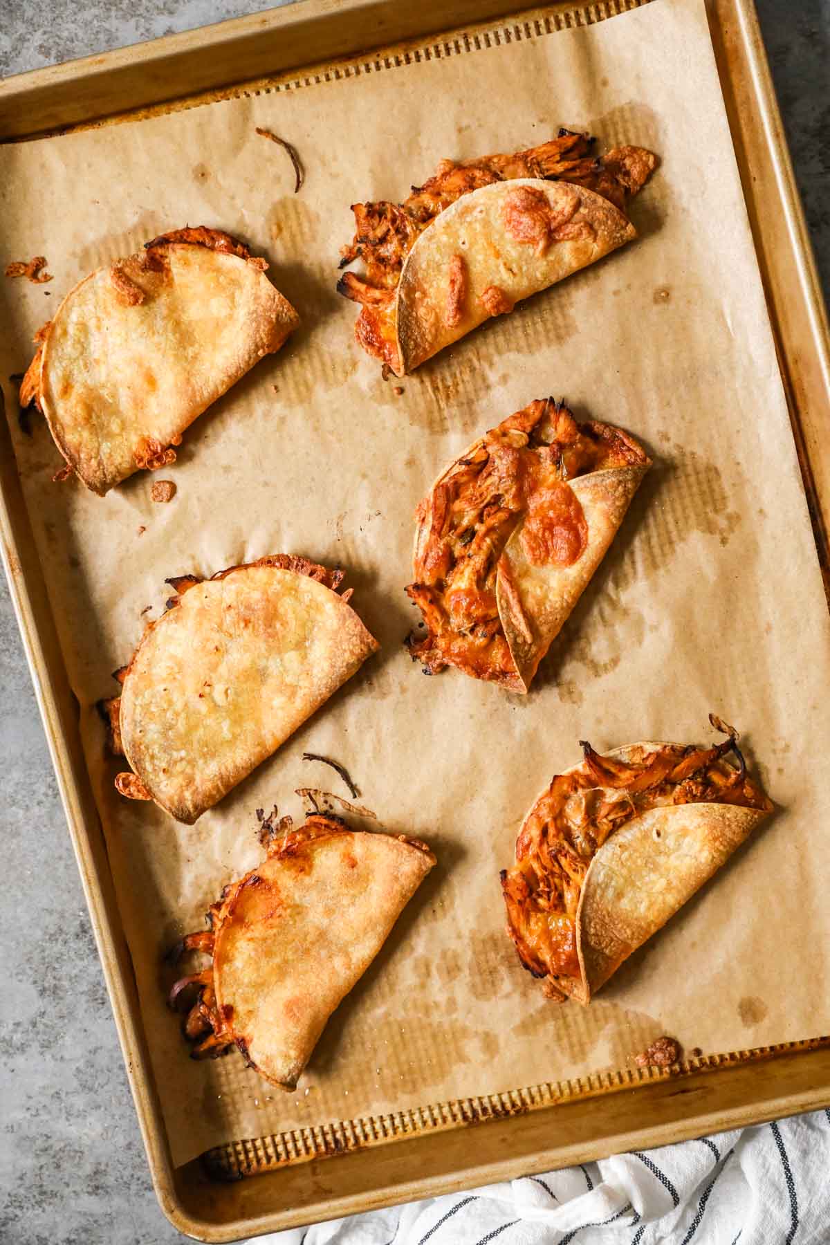 Oven crispy chicken tacos over elevated landscape on parchment lined baking tray.