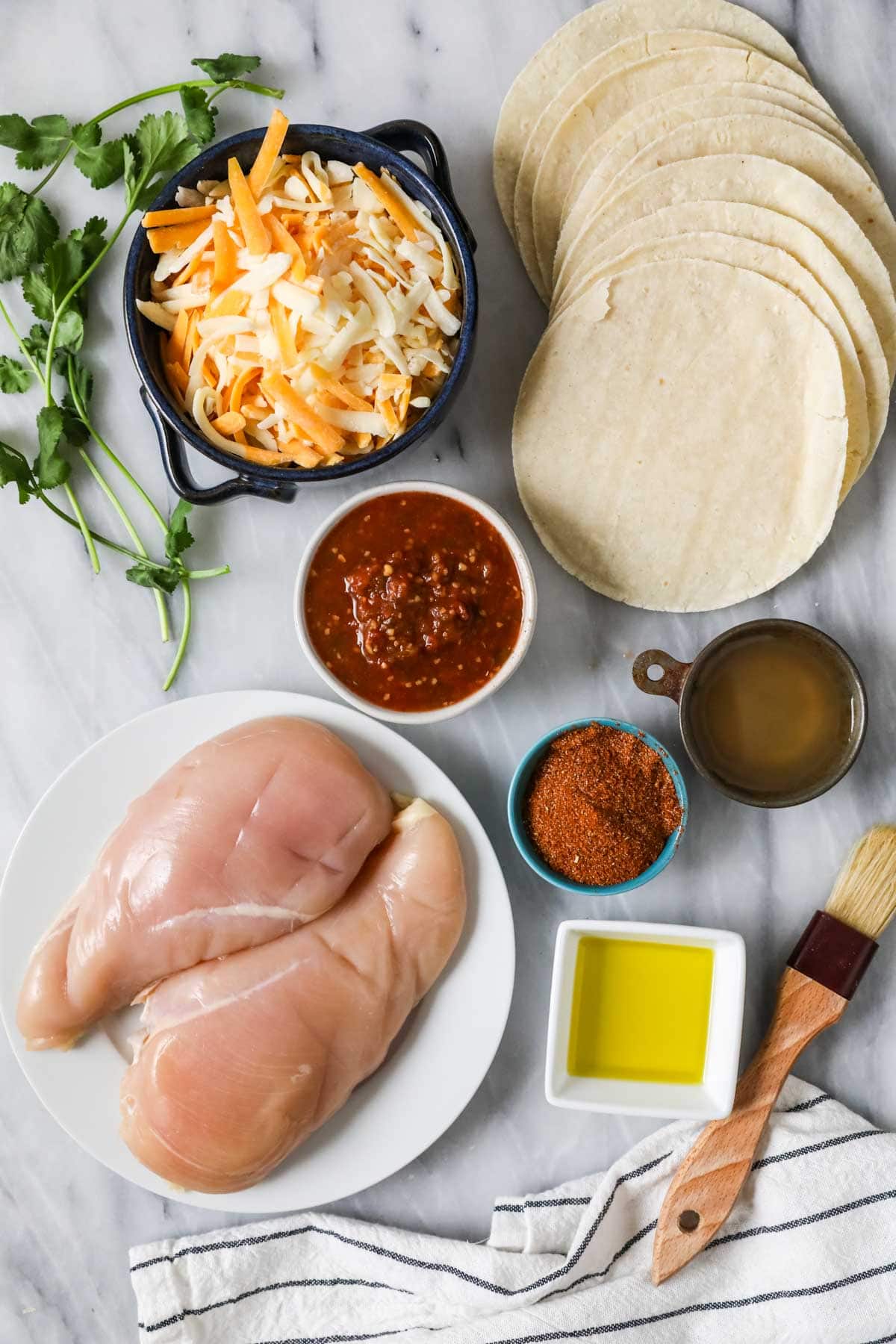 Elevated landscape of ingredients including tortillas, chicken breasts, salsa, cheese and more.