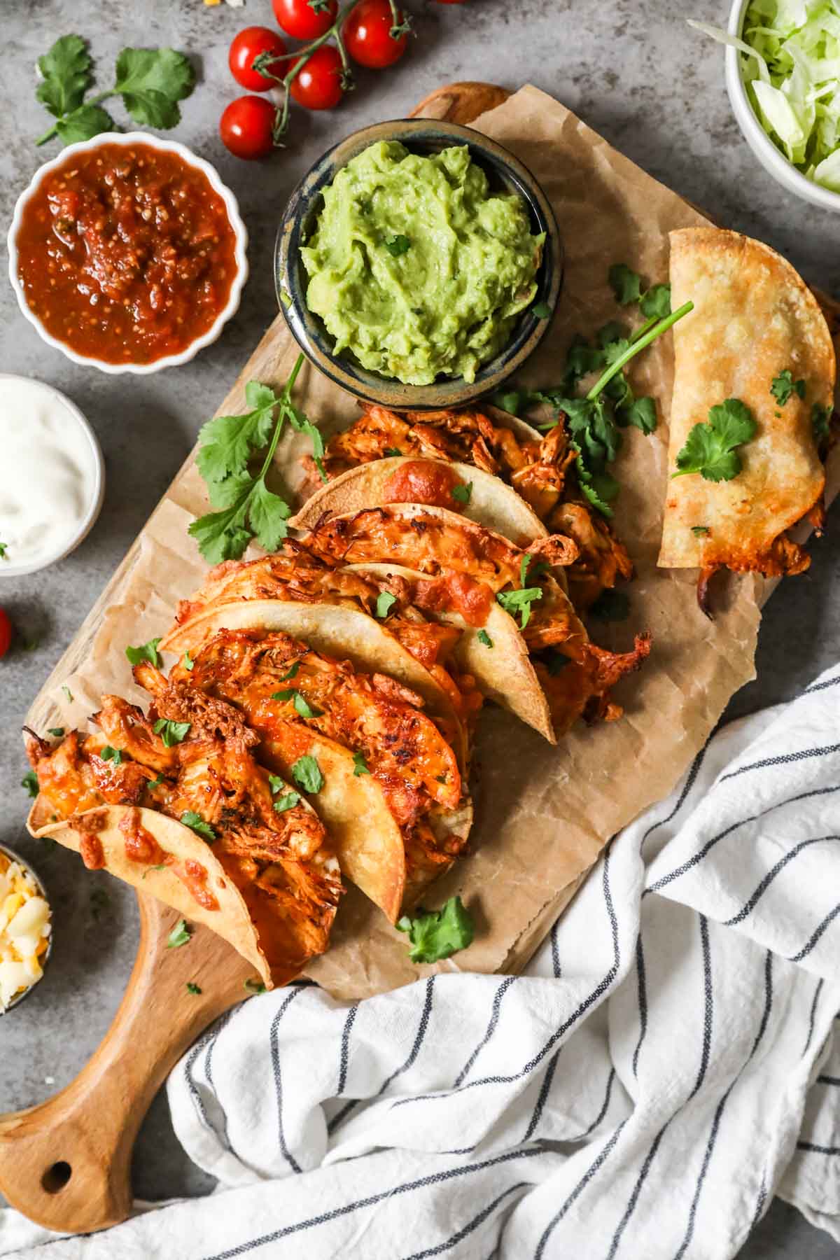 Side of wooden tacos over elevated landscape on wooden cutting board, guacamole, salsa, sour cream and cheese.