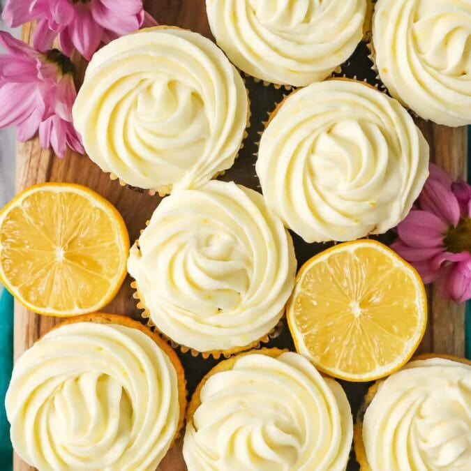 Overhead view of cupcakes frosted with lemon cream cheese frosting among lemon halves.
