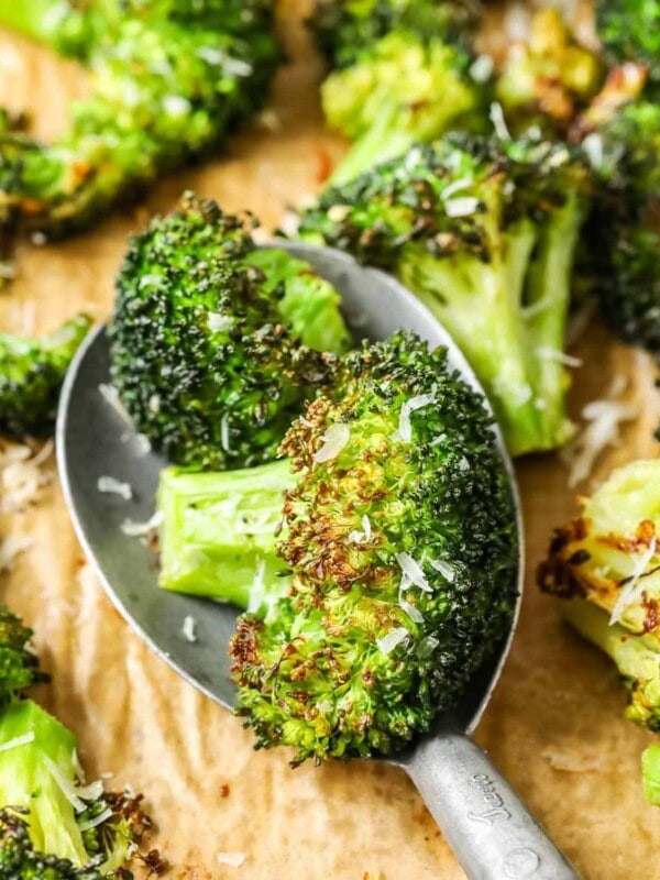 Spoonful of roasted broccoli being scooped off a baking sheet.