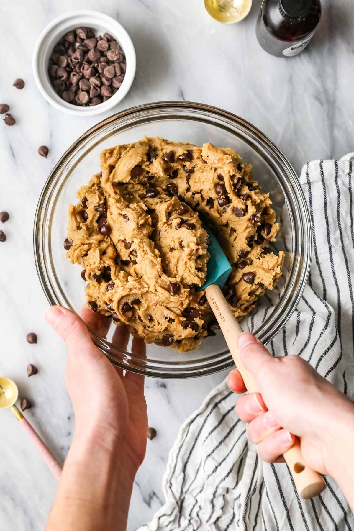 Overhead view of a bowl of chocolate chip cookie dough being stirred with a spatula.