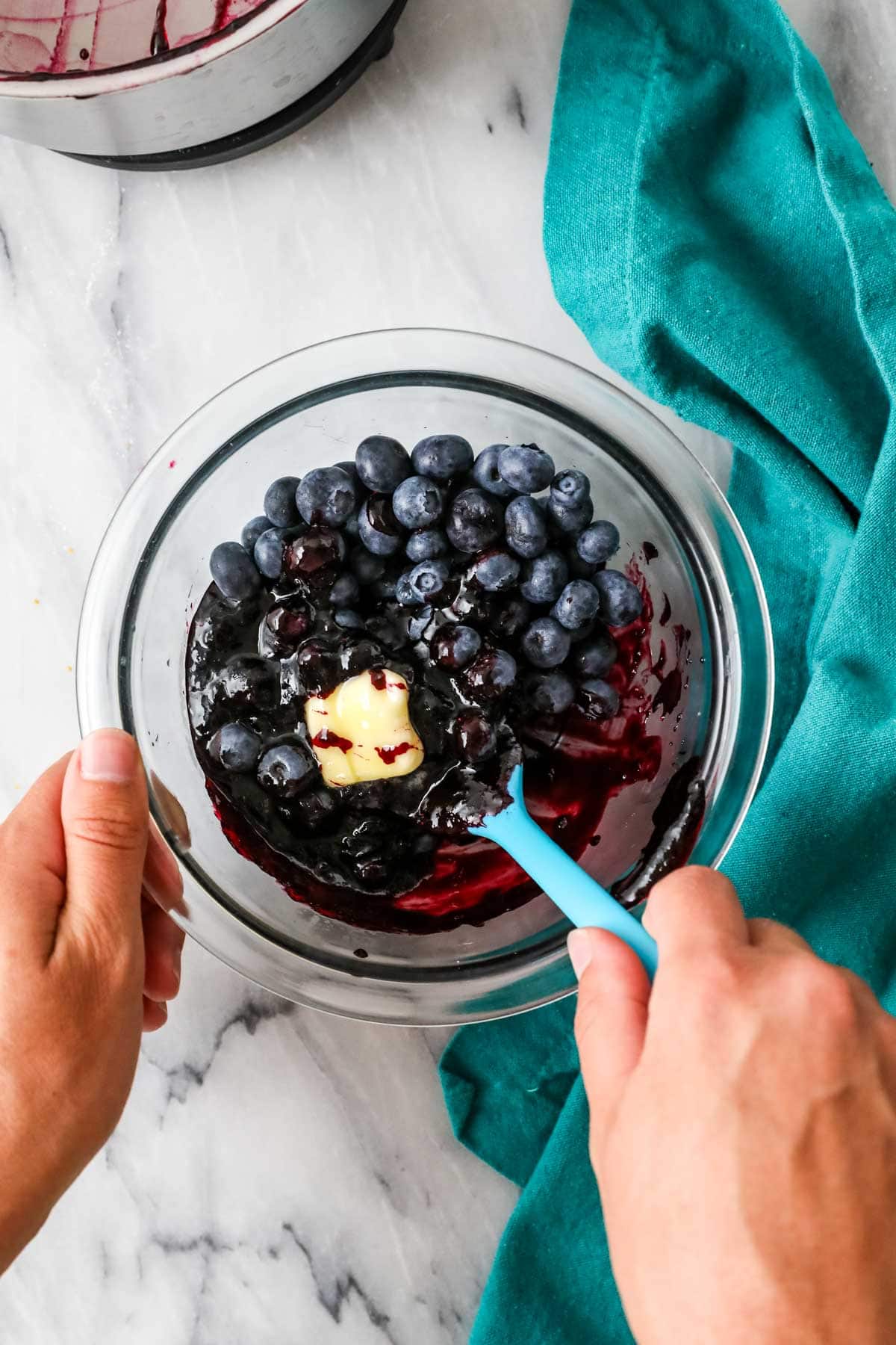 Butter and fresh blueberries being stirred into a cooked blueberry sauce mixture.