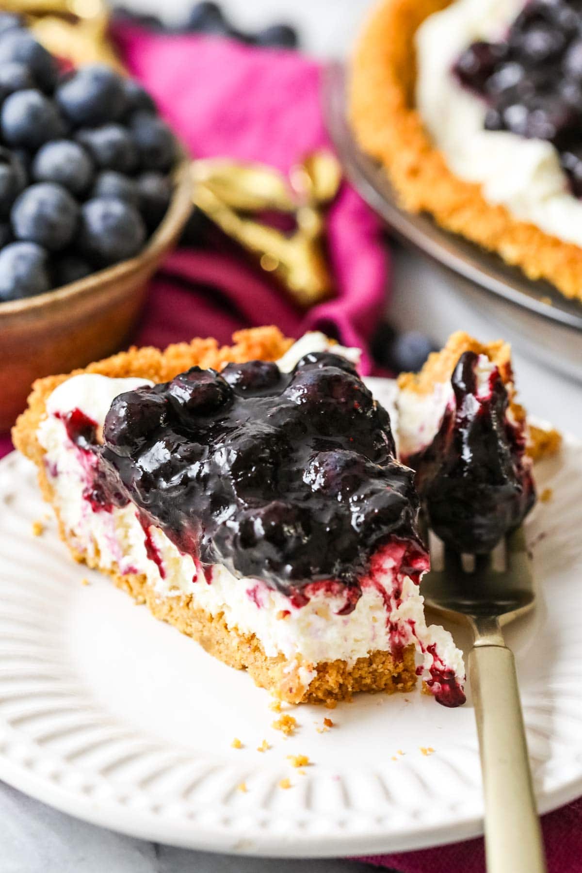 Forkful of blueberry cream cheese pie resting on a plate beside the slices.