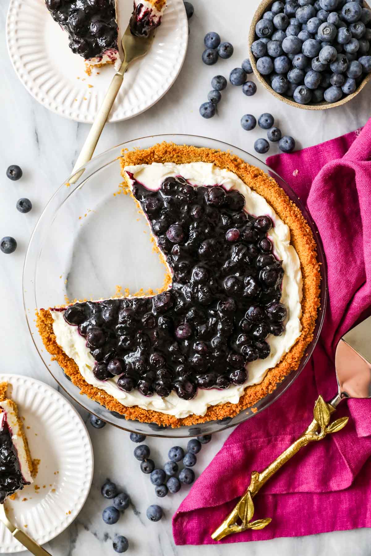 Overhead view of slices missing from a pie made with a cream cheese filling and blueberry topping.