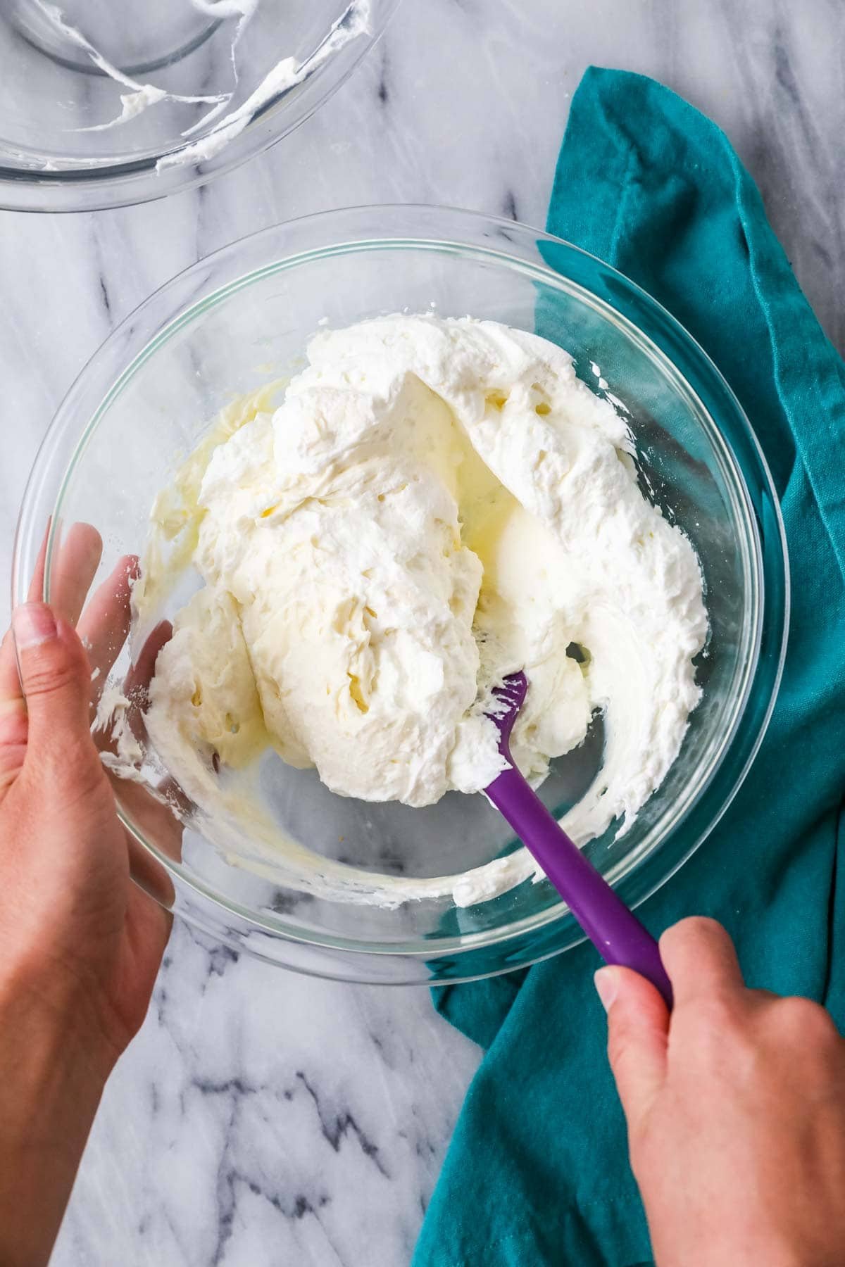 Spatula folding whipped cream into a cream cheese mixture.