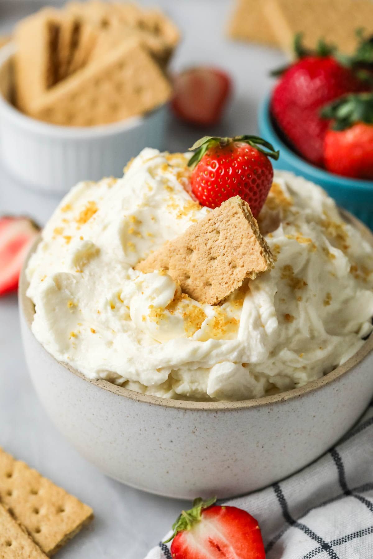 Bowl of cheesecake dip with graham cracker crumbs, a graham cracker, and a strawberry on top.