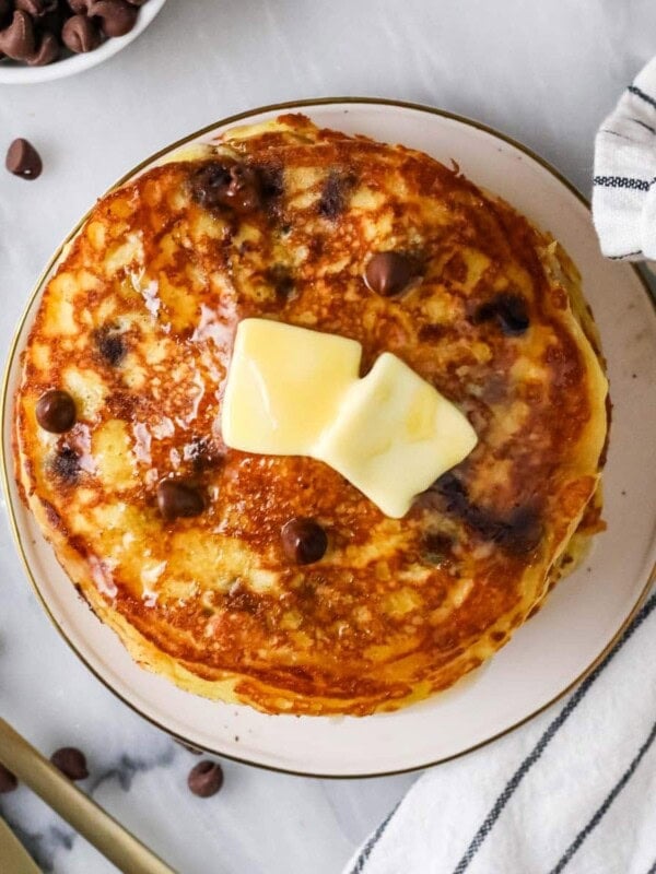 Overhead view of a stack of chocolate chip pancakes topped with butter and syrup.