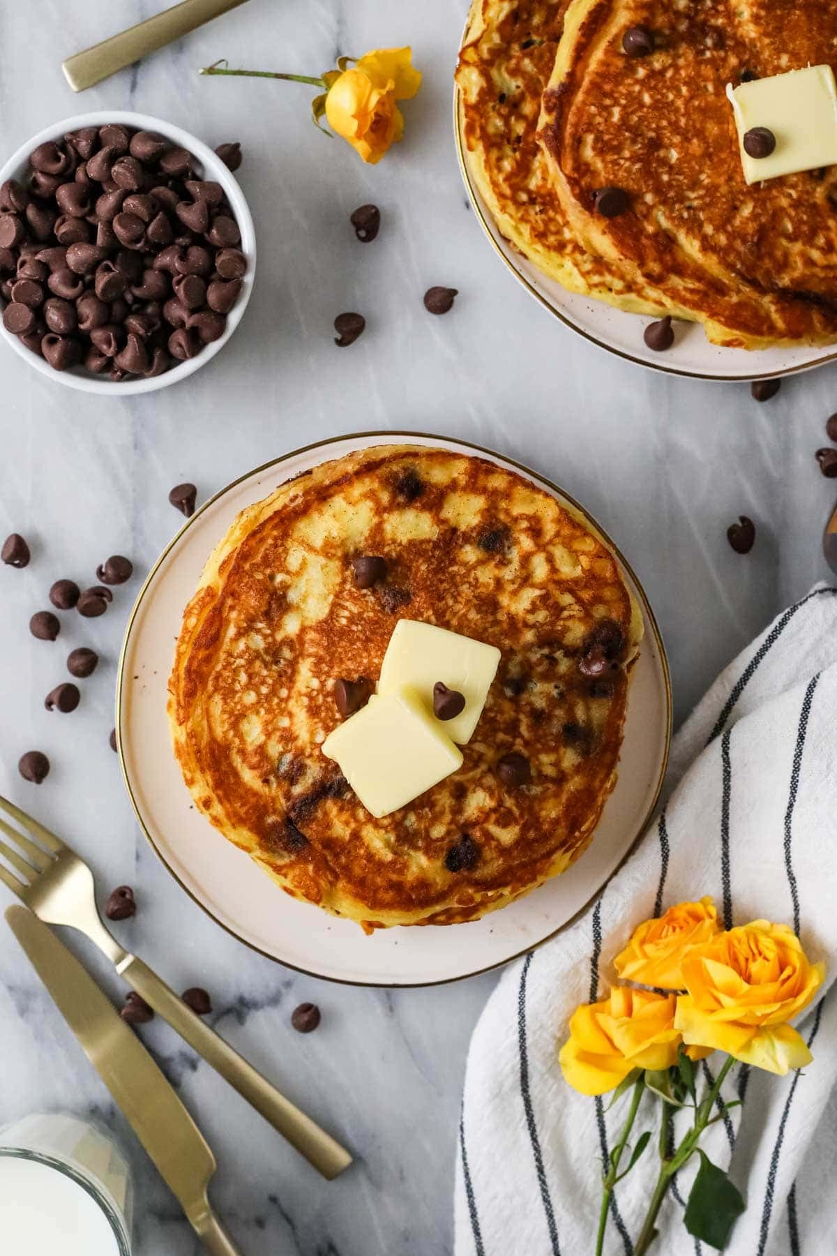 Overhead view of a stack of chocolate chip pancakes topped with butter and syrup.