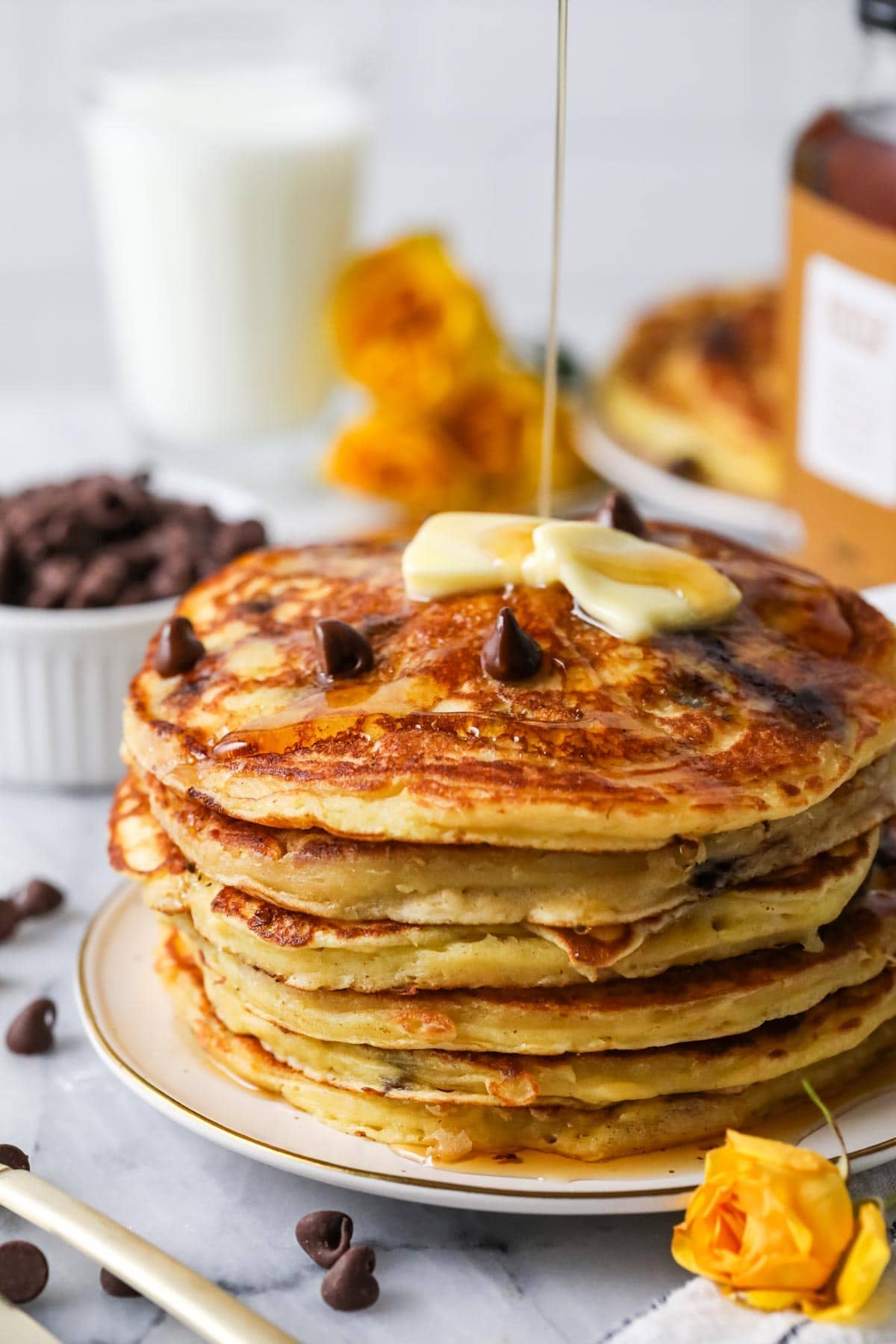 Maple syrup being drizzled over a stack of chocolate chip pancakes.