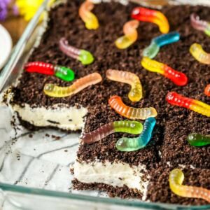 Slices missing from a pan of homemade dirt cake made with Oreo cookie crumbs, a cream cheese filling, and gummy worms.