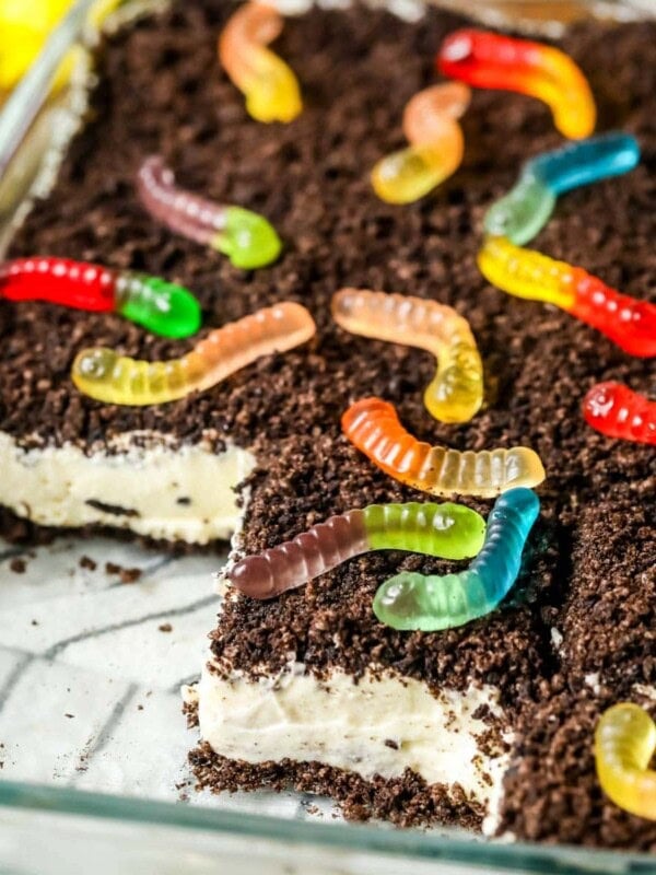 Slices missing from a pan of homemade dirt cake made with Oreo cookie crumbs, a cream cheese filling, and gummy worms.