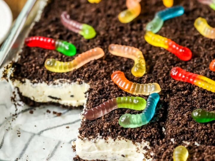 Slices missing from a pan of homemade dirt cake made with Oreo cookie crumbs, a cream cheese filling, and gummy worms.