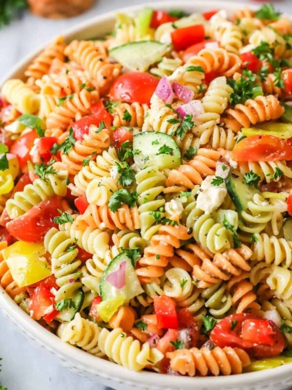 Bowl of pasta salad made with tri-color rotini, veggies, and feta cheese.