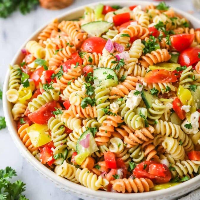 Bowl of pasta salad made with tri-color rotini, veggies, and feta cheese.