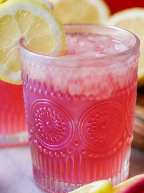 Glass of pink lemonade garnished with a lemon slice.
