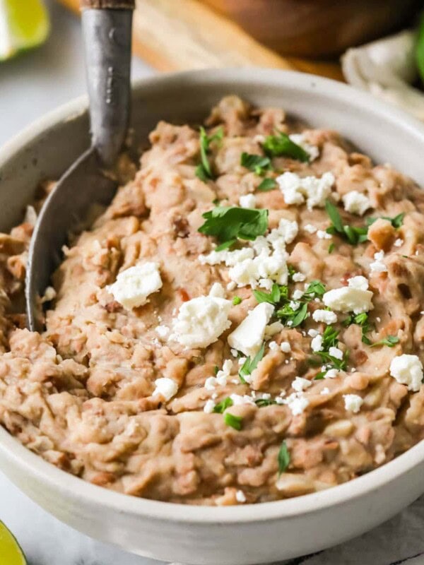 Bowl of homemade refried beans topped with cheese and cilantro.