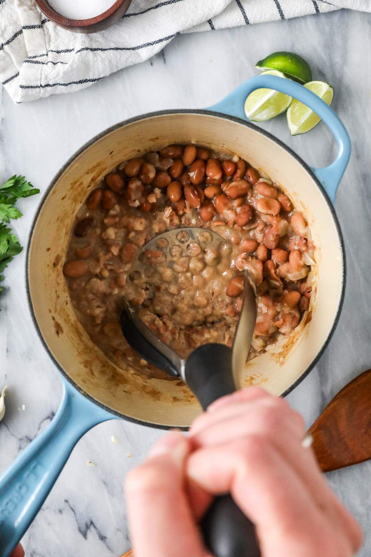 Overhead view of pinto beans being mashed in a pot.