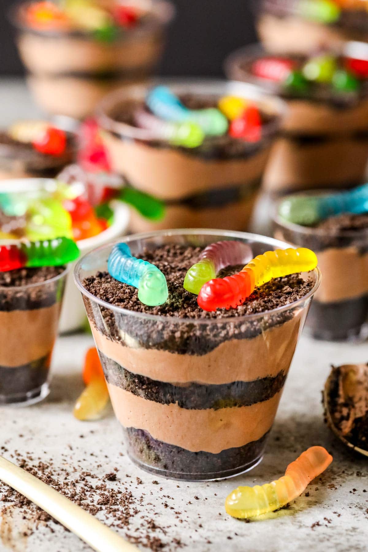 Dirt cups with distinct layers of crushed Oreos and pudding and gummy worms on top.