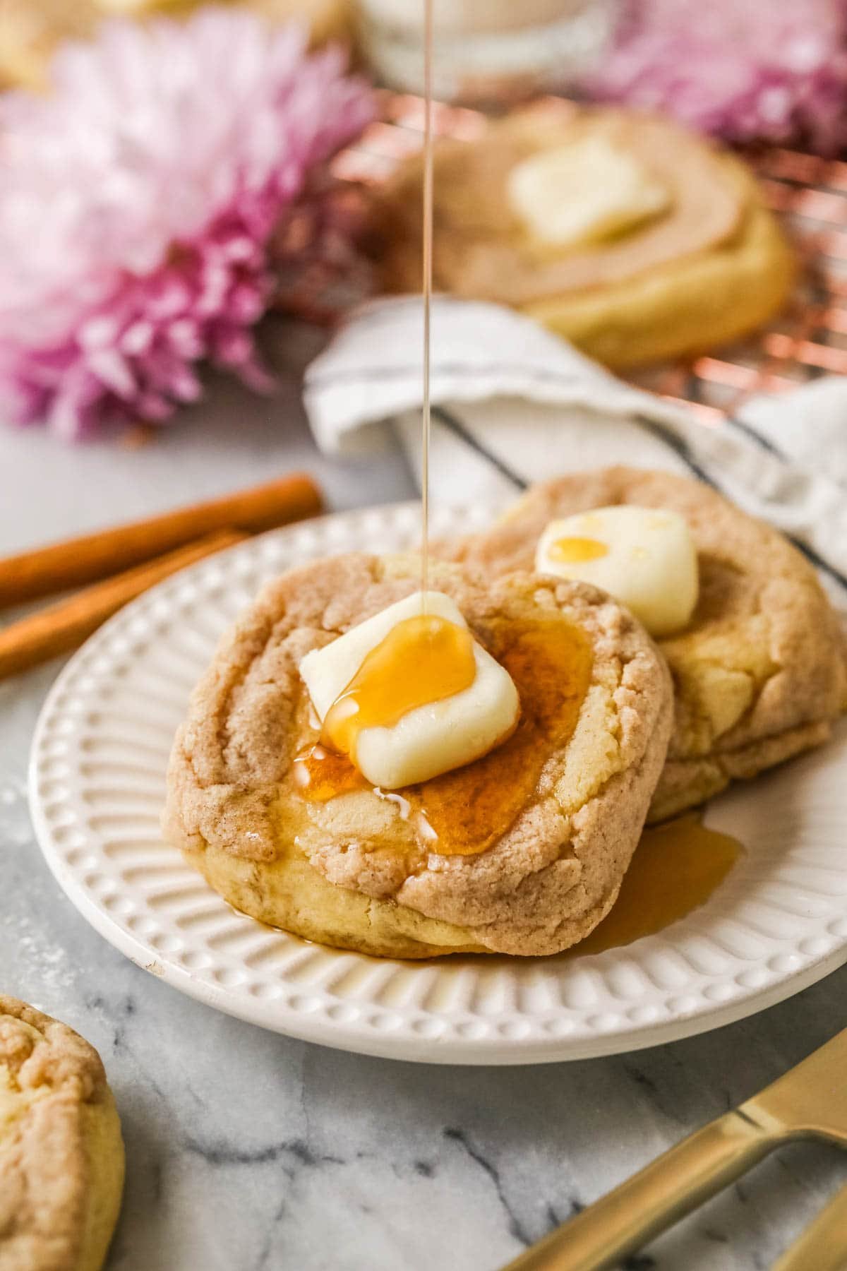 French toast cookies with a buttercream pat of butter and syrup being drizzled overtop.