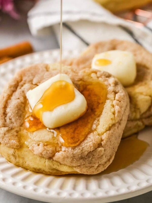 French toast cookies with a buttercream pat of butter and syrup being drizzled overtop.