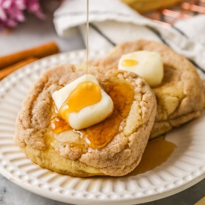 French toast cookies with a buttercream pat of butter and syrup being drizzled overtop.