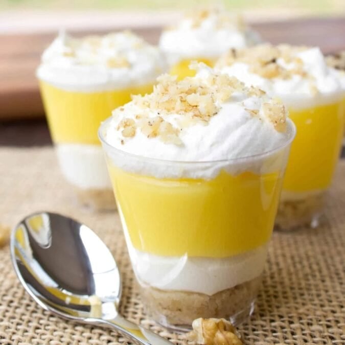Lemon lush dessert shooters topped with Cool Whip and crushed walnuts.