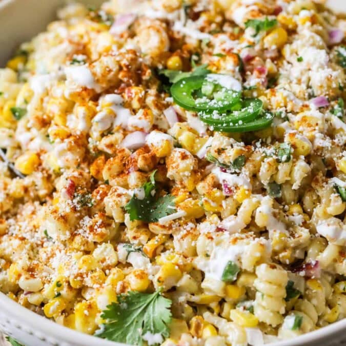 Close-up view of a Mexican street corn pasta salad topped with cilantro, jalapeno, cotija cheese, and chili powder.
