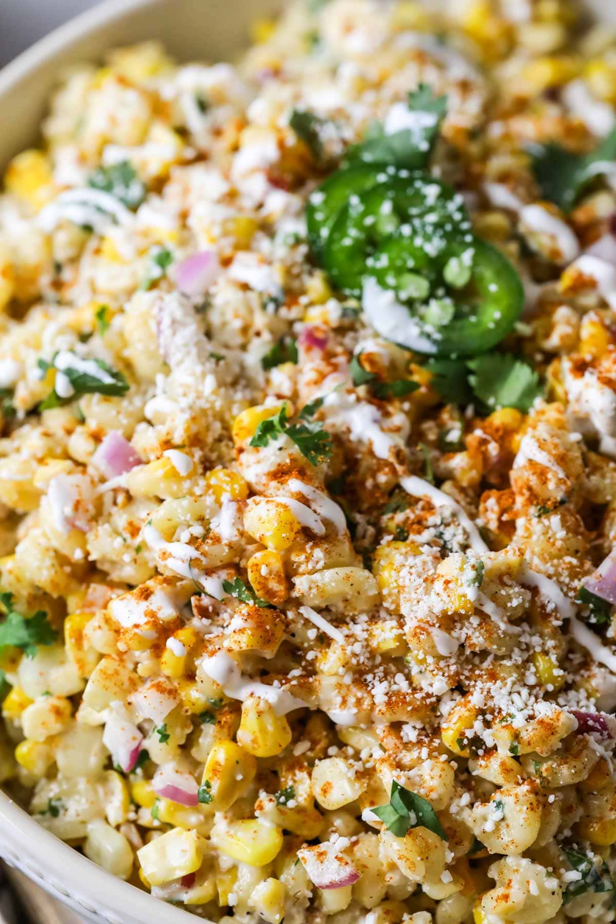 Close-up view of a Mexican street corn pasta salad topped with cilantro, jalapeno, cotija cheese, and chili powder.