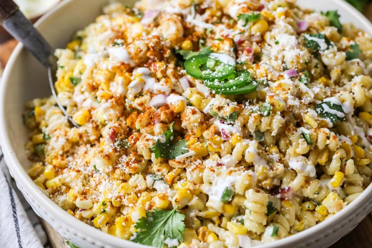 Close-up view of a Mexican street corn pasta salad topped with cilantro, jalapeno, cotija cheese, and chili powder.