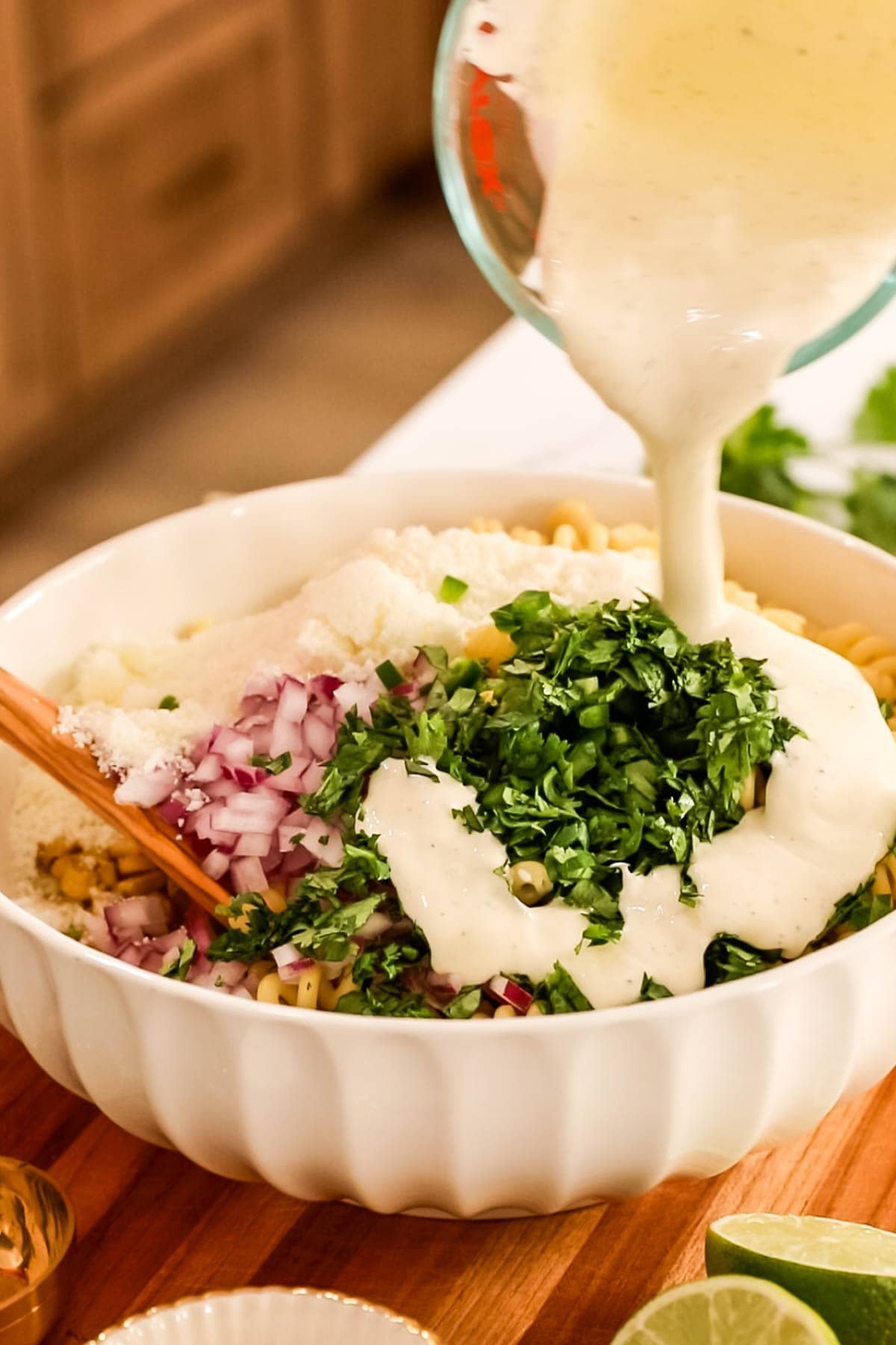 Dressing being poured over a pasta salad made with corn, red onion, jalapeno, and more.