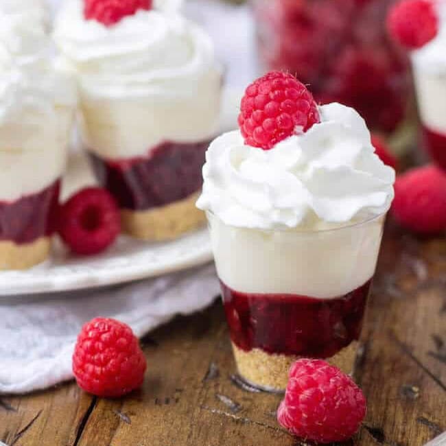 Close-up view of a dessert shooter made with graham cracker crumbs, raspberry filling, no-bake cheesecake, and whipped cream.