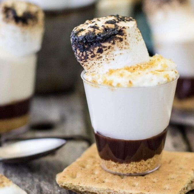 Shot glass dessert with a layers of graham cracker crumbs, ganache, and marshmallow cheesecake.