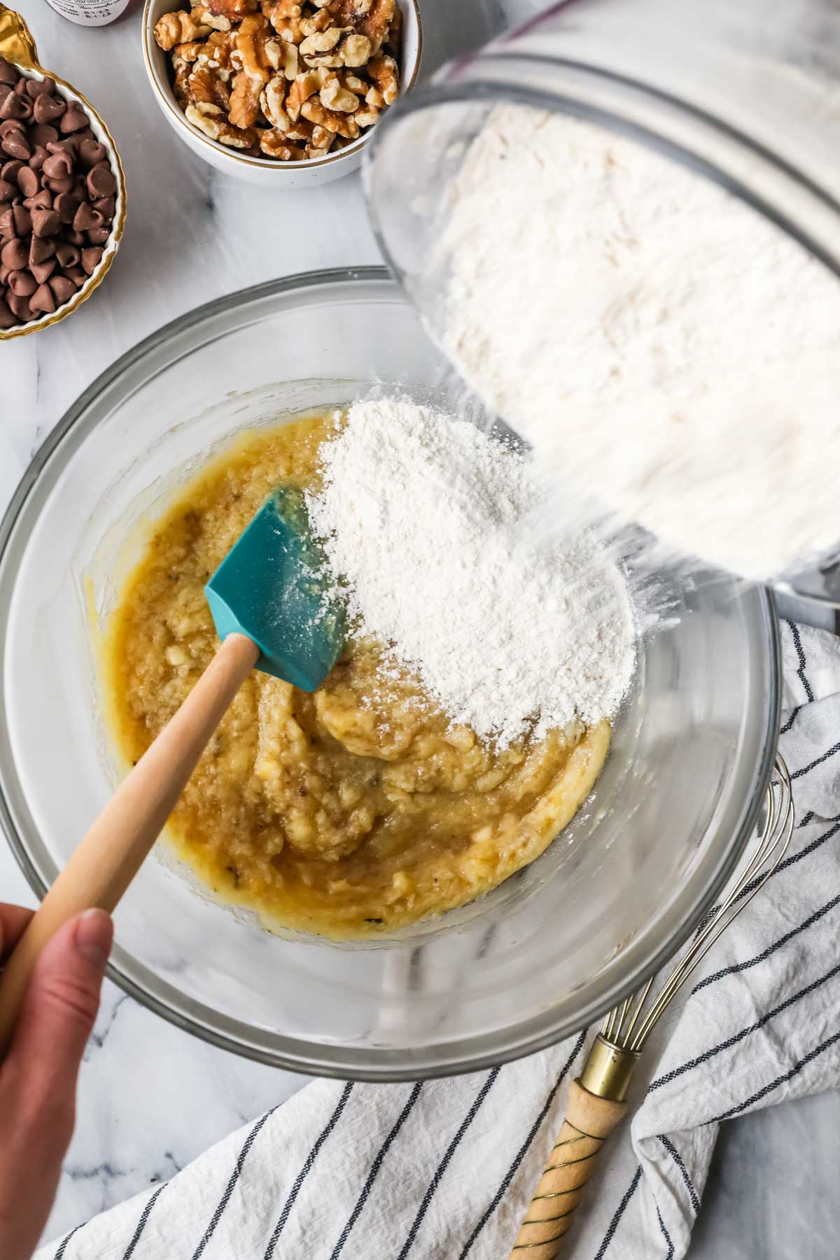 Overhead view of dry ingredients being added to a mashed banana mixture.