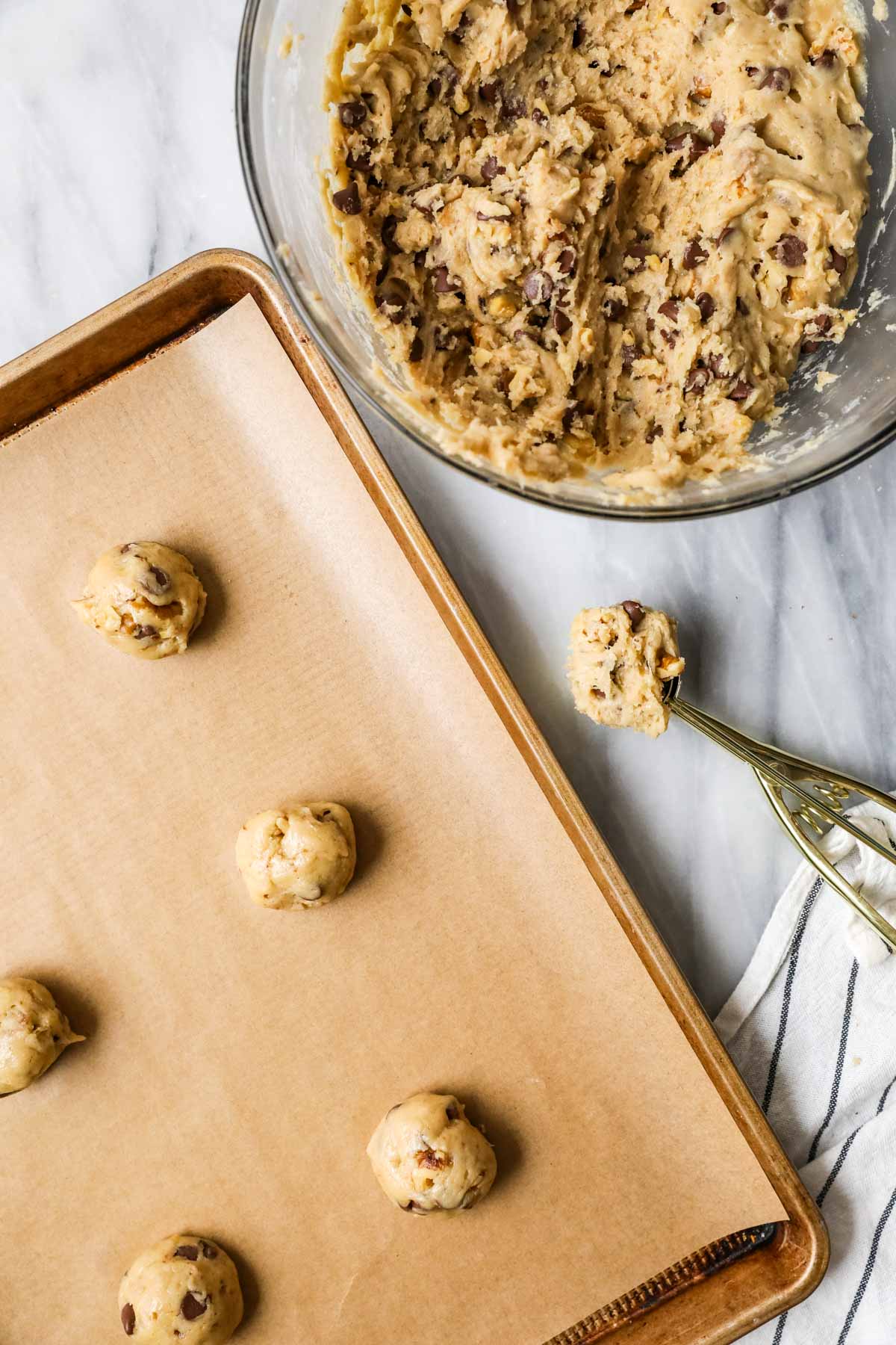 Overhead view of cookie dough balls made with bananas and chocolate chips being scooped and rolled on a cookie sheet.