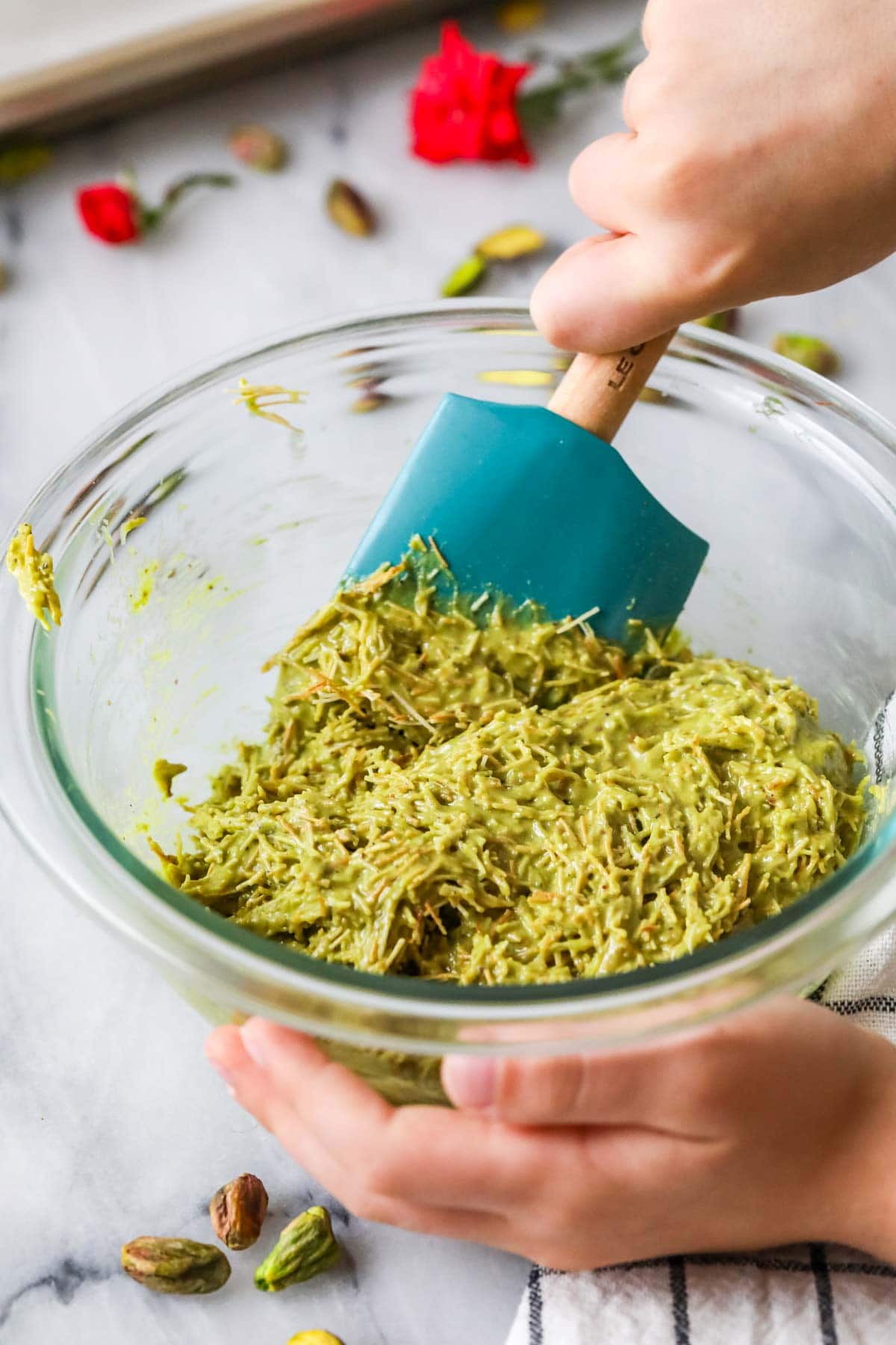 Spatula stirring pistachio cream and kataifi together in a bowl.