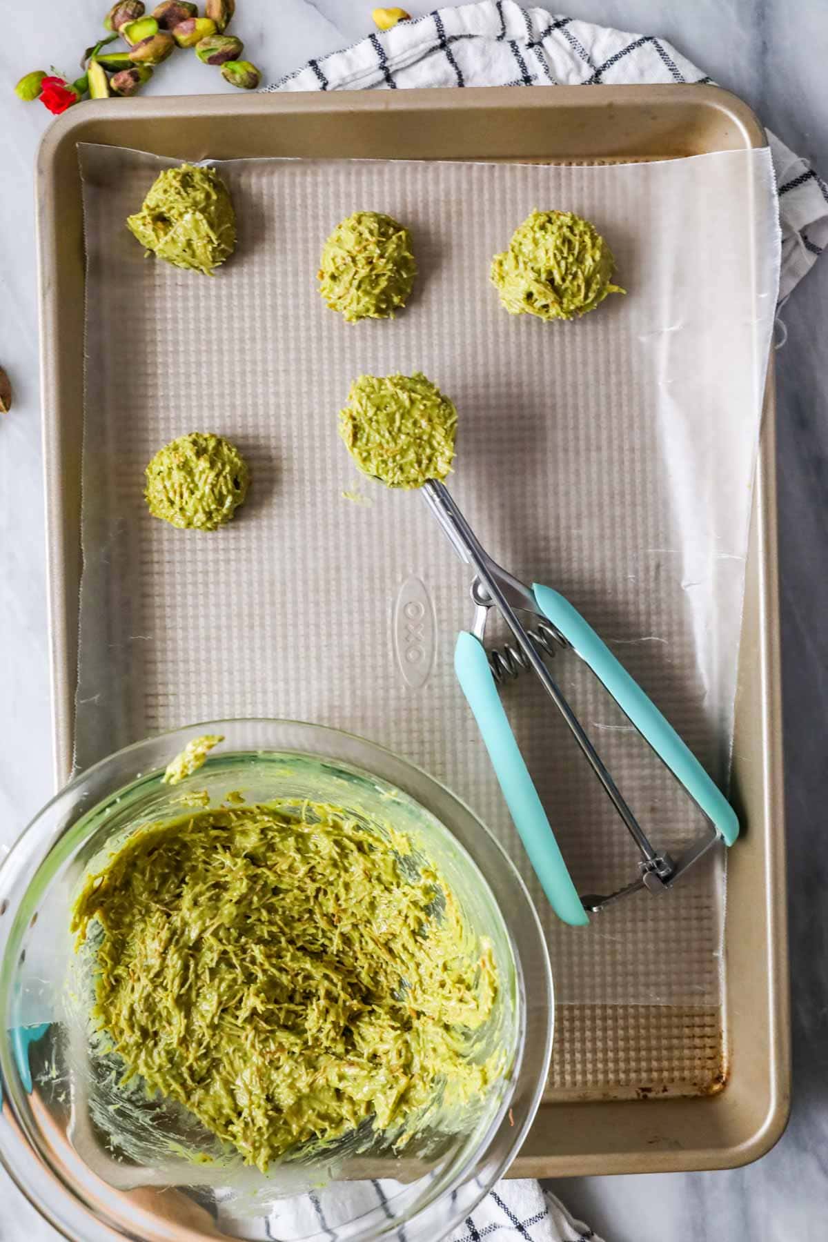 Overhead view of scoops of a pistachio and kataifi mixture being dropped on a lined cooking sheet.