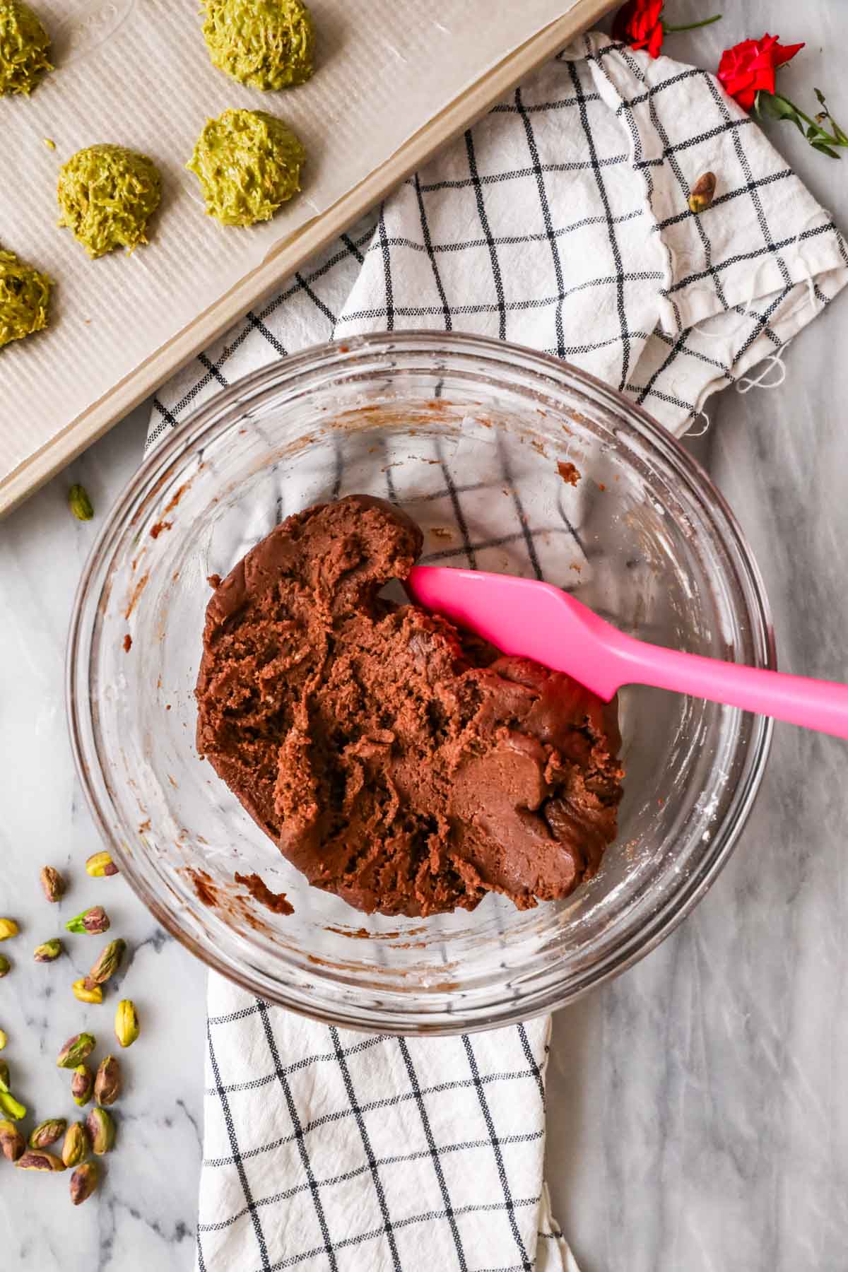 Overhead view of a bowl of chocolate cookie dough being stirred with a pink spatula.