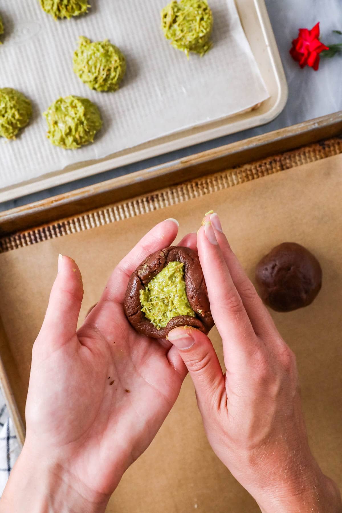 Hands folding chocolate cookie dough around a frozen pistachio filling.