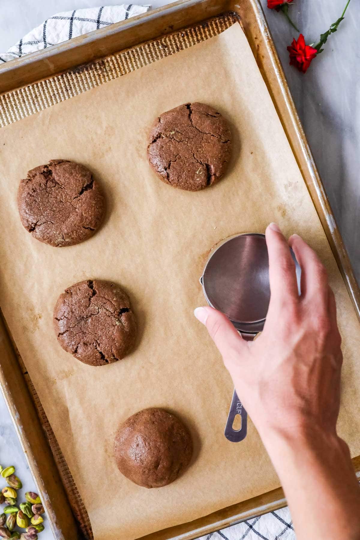 Flattening Dubai cookies with a measuring cup after baking.