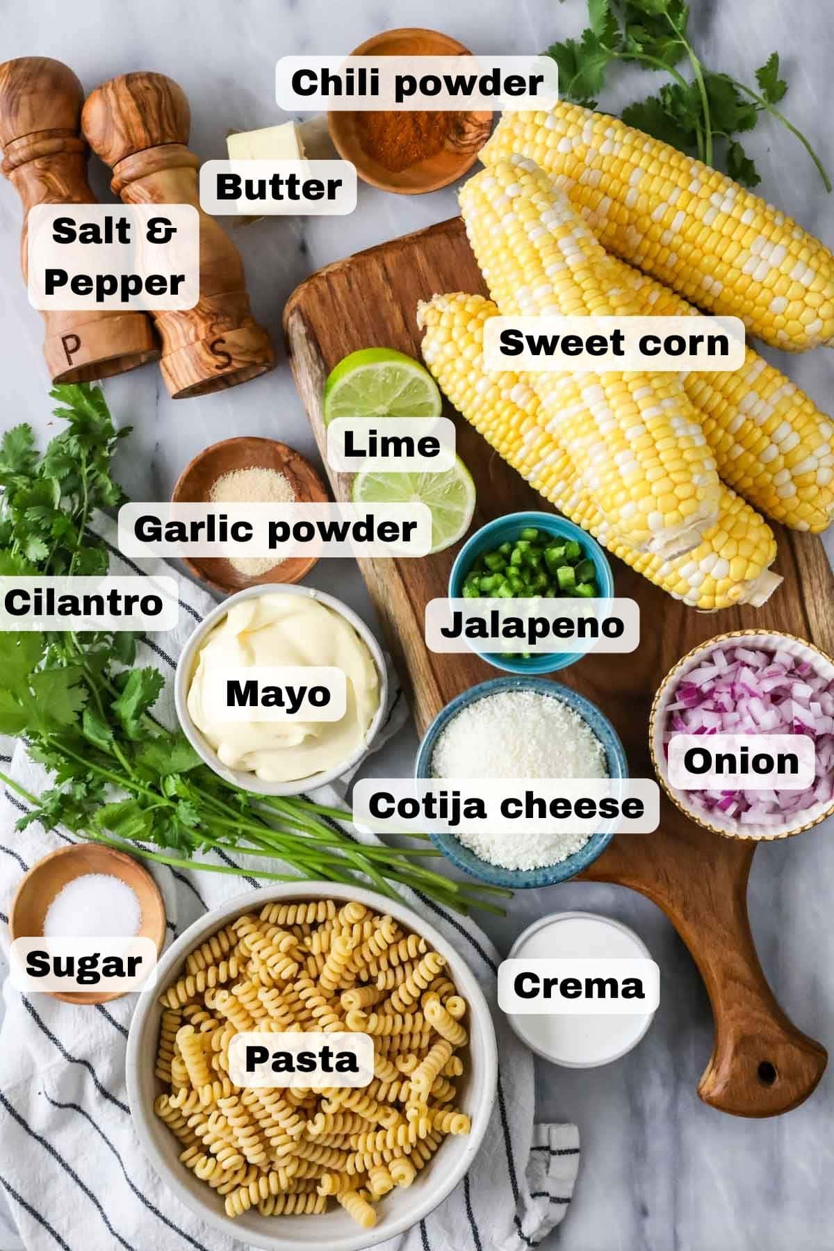 Overhead view of (labeled) ingredients for Mexican street corn pasta salad including corn on the cob, cilantro, red onion, and more.