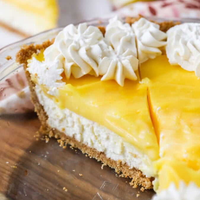 Slice of lemon cream cheese pie topped with whipped cream in a pie plate.