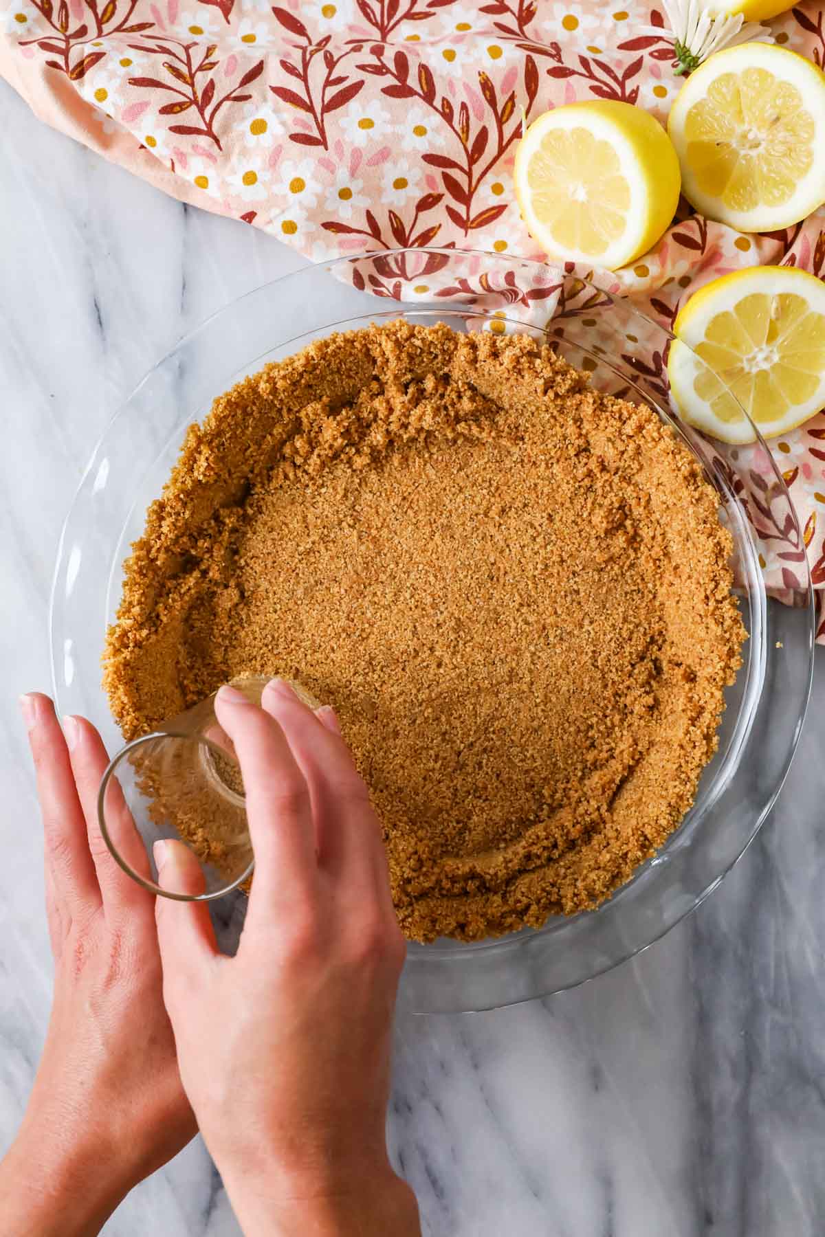 Overhead view of graham cracker crumbs being pressed into a pie dish.