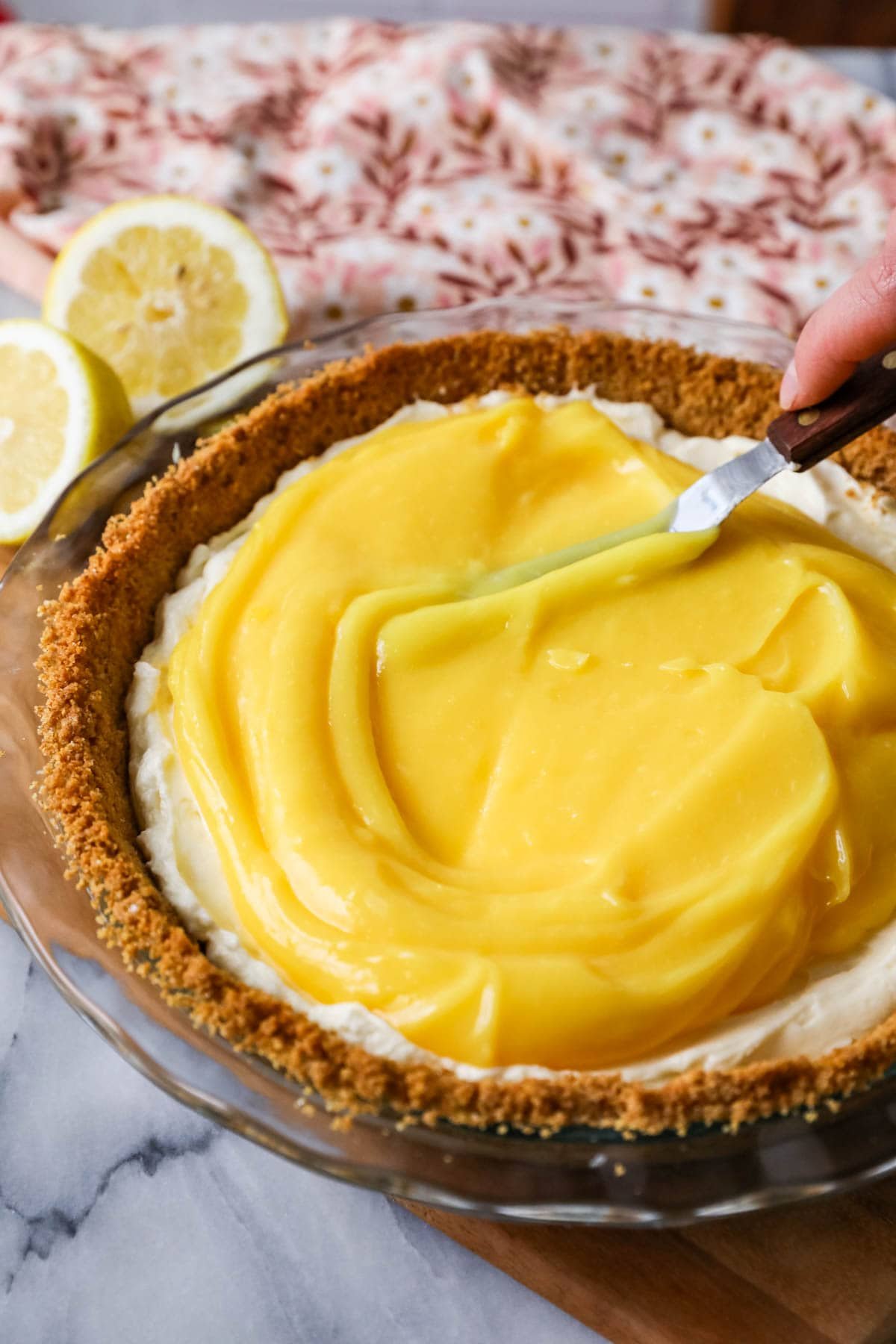 Lemon topping being spread over a cream cheese filling in a graham cracker pie crust.