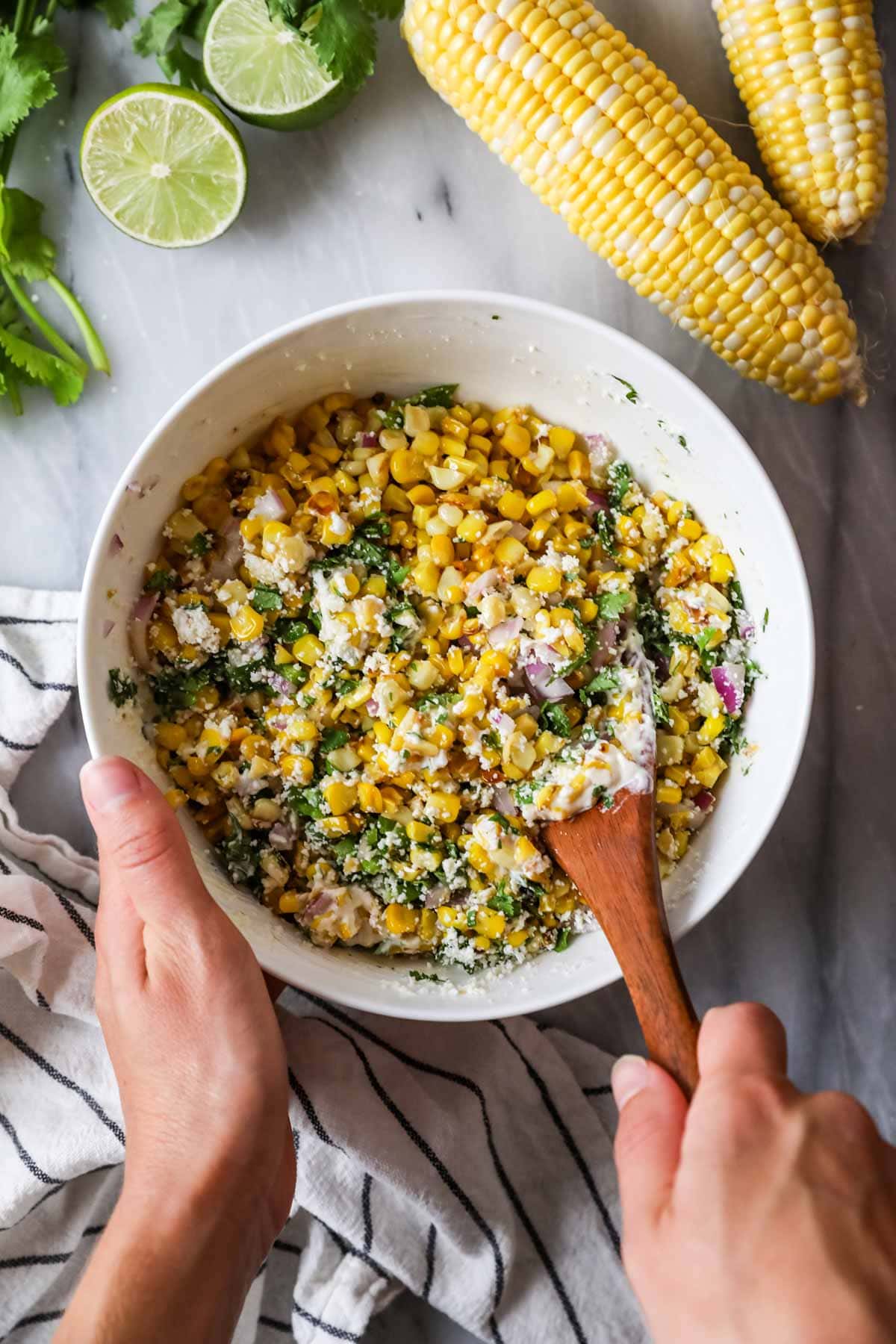 Overhead view of a bowl of corn being stirred together with cilantro, cotija cheese, red onion, and more.
