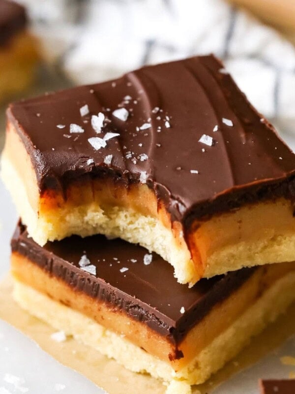 Two square slices of millionaire's shortbread topped on top each other, a bite missing to show chewy caramel center. Topped with sea salt.