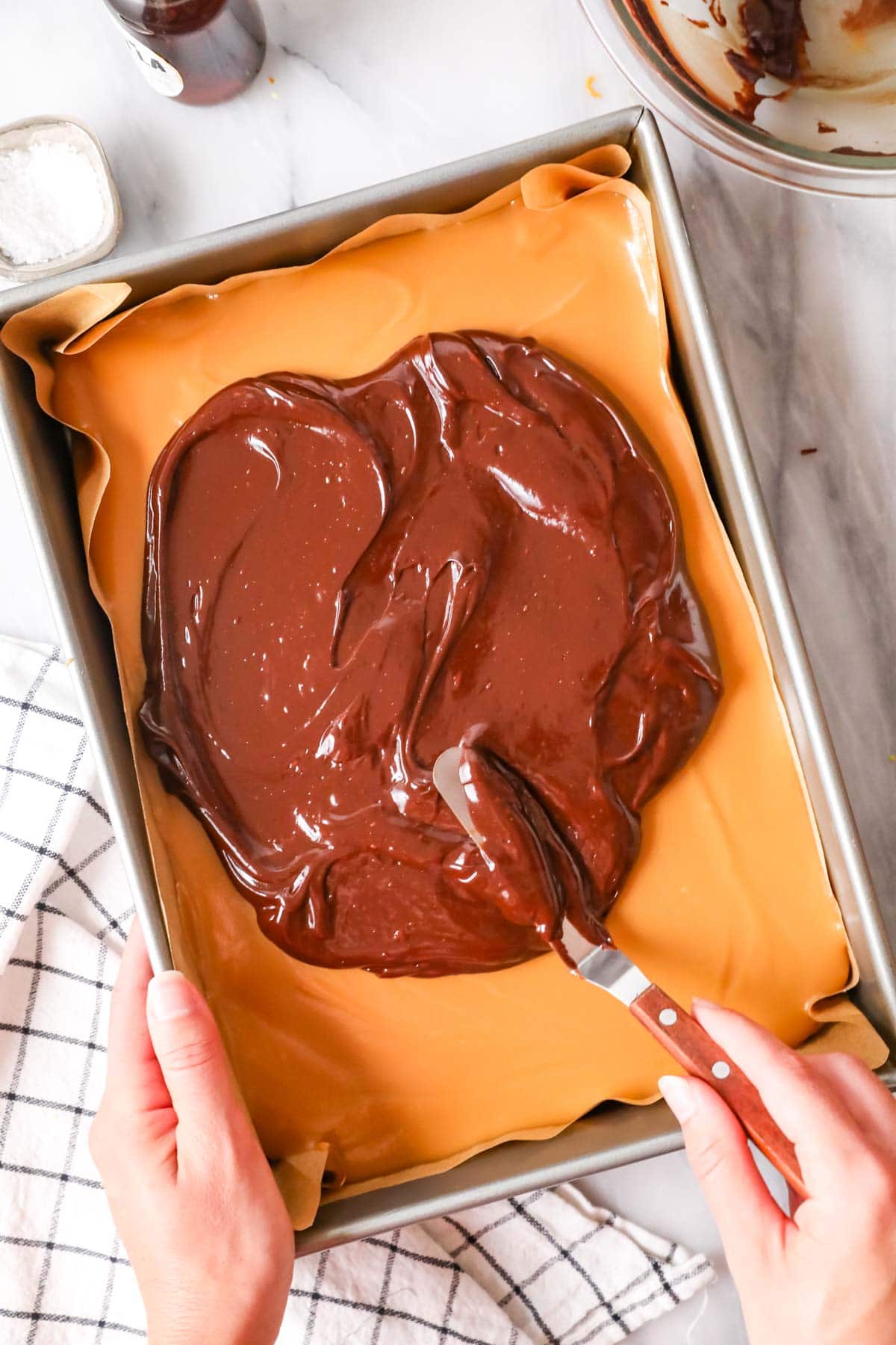 Spreading ganache over cooled caramel layer of millionaire's shortbread.
